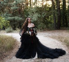 a woman in a black dress standing on a dirt road