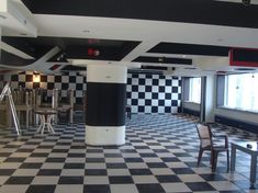 an empty room with checkered floor and black and white tiles on the walls, tables and chairs