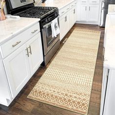 a kitchen with white cabinets and an area rug on the floor in front of the stove