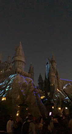 the hogwarts castle is lit up at night with people standing around looking on