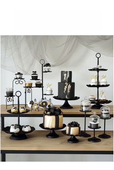 a table topped with lots of cakes and cupcakes on top of black stands