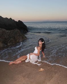 a woman sitting on top of a sandy beach next to the ocean