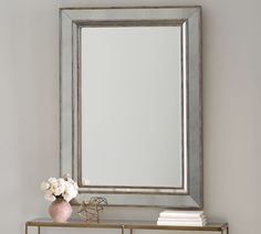 a mirror sitting on top of a table next to a vase with flowers