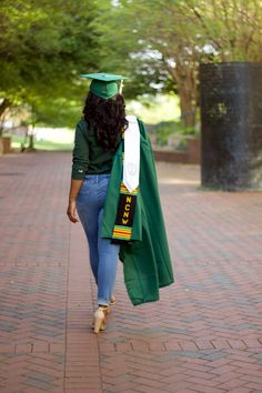 a woman walking down the street wearing a green graduation gown and cap with her name on it