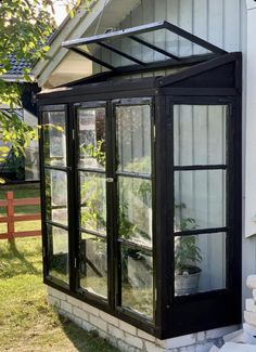 a small greenhouse in front of a white house with black trim and glass doors on the side