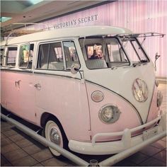 a pink and white vw bus parked in front of a building with people inside