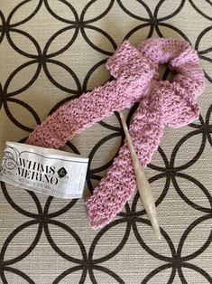 a pink crocheted knitted scarf laying on top of a table next to a knitting needle