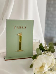 a table number one card with white flowers on it and a candle next to it