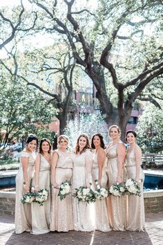 a group of women standing next to each other in front of a tree and water fountain