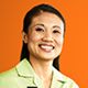 a woman in a green shirt smiling at the camera with an orange wall behind her