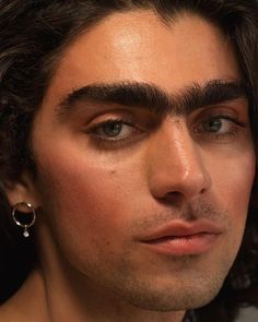 a close up of a person with long hair and piercings on his ear wearing earrings