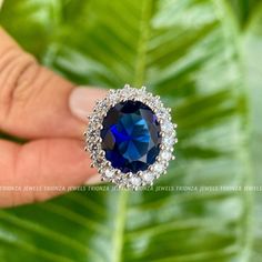 a person holding a blue ring on top of a green leaf with diamonds around it