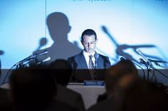 a man in a suit and tie standing at a podium with microphones behind him