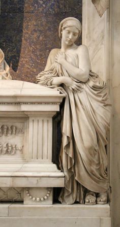 a statue of a woman sitting on top of a white bench next to a wall