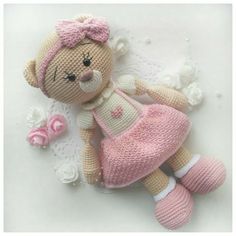 a stuffed teddy bear wearing a pink dress laying on a doily next to flowers