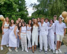 a group of young people standing next to each other in front of trees and bushes