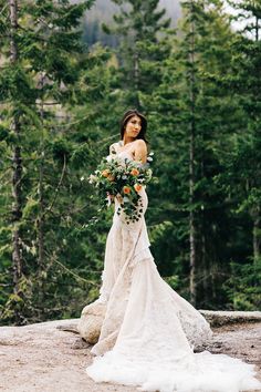 a woman standing on top of a rock holding a bouquet of flowers in her hand