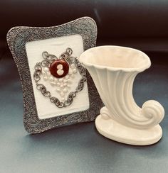 a white vase sitting on top of a table next to a decorative frame with a button