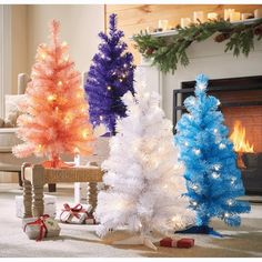 three different colored christmas trees sitting in front of a fireplace