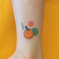 an orange tattoo on the ankle with japanese characters and words above it, in front of a yellow background