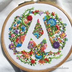 an embroidered peace sign with colorful flowers and leaves on white fabric in a wooden frame