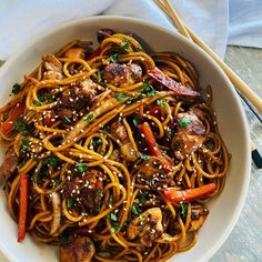 a white bowl filled with noodles and meat on top of a table next to chopsticks