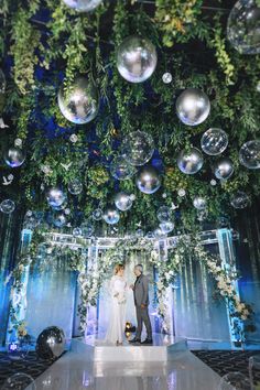 a bride and groom standing under bubbles in front of a wall with greenery on it