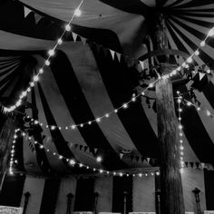 black and white photograph of lights strung from the ceiling in a tent with large striped walls