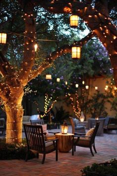 an outdoor dining area with lights strung around the tree and patio furniture set up for dinner