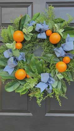 a wreath with oranges and green leaves hanging on a front door, decorated with blue ribbon