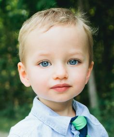 a young boy wearing a blue shirt and green tie with trees in the back ground