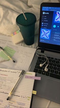 an open laptop computer sitting on top of a bed next to a cup and pen