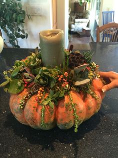 a candle is sitting on top of a pumpkin filled with greenery and other plants