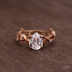 an engagement ring with a pear shaped diamond in the center and leaves around it, on a brown background