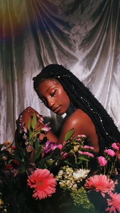 a woman with long braids sitting in front of flowers