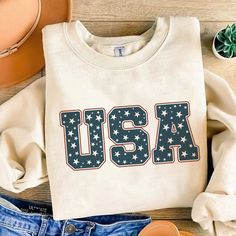 an american flag sweatshirt and jeans are laid out on a wooden table with cowboy hats