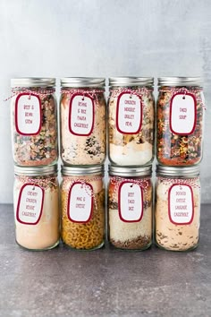 six jars filled with different types of food and labeled labels on the lids, sitting on a table