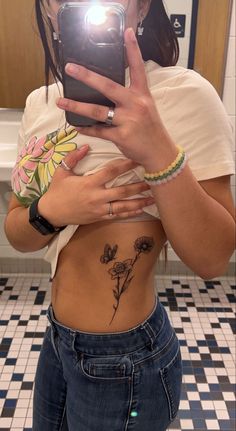 a woman taking a selfie in the bathroom with her cell phone and flower tattoo on her stomach