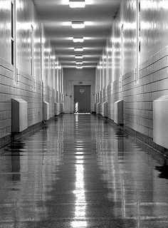 a long hallway with tiled walls and flooring in black and white colors, leading to an exit door