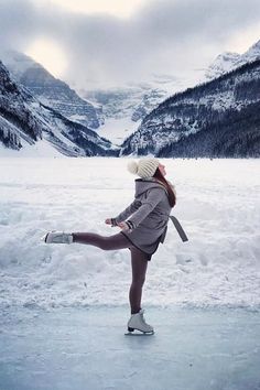 a woman skating on an ice rink in front of mountains and snow covered ground with her legs spread out