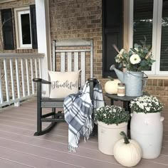 a porch with white pumpkins and flowers on the front steps, next to a rocking chair