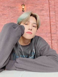 a young man with green hair sitting in front of a brick wall