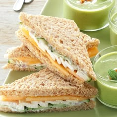 two sandwiches cut in half on a green plate next to cups of juice and spoons