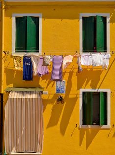 clothes hanging out to dry in front of a yellow building with green shutters and windows