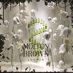 a window display with white flowers and green bottles in the background that says motton brown london