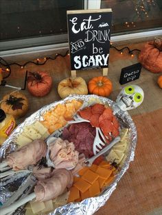 an assortment of meats and cheeses on tin foil with a sign that says eat drink and be scary