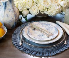 a table with plates, silverware and vases filled with white flowers on it