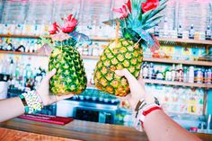 two pineapples being held up in front of a bar