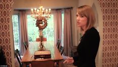 a woman standing in front of a dining room table with a chandelier hanging from the ceiling