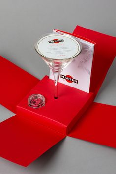 a martini glass sitting on top of a red box with a card in the middle